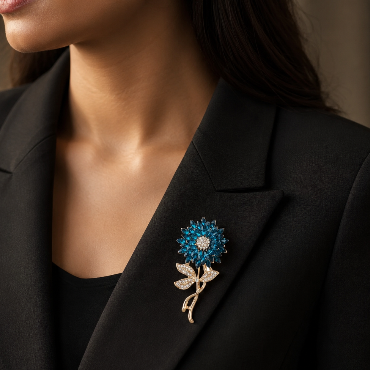 A close-up of a woman wearing a black blazer and black top, featuring a blue and gold flower-shaped brooch pinned to the lapel.