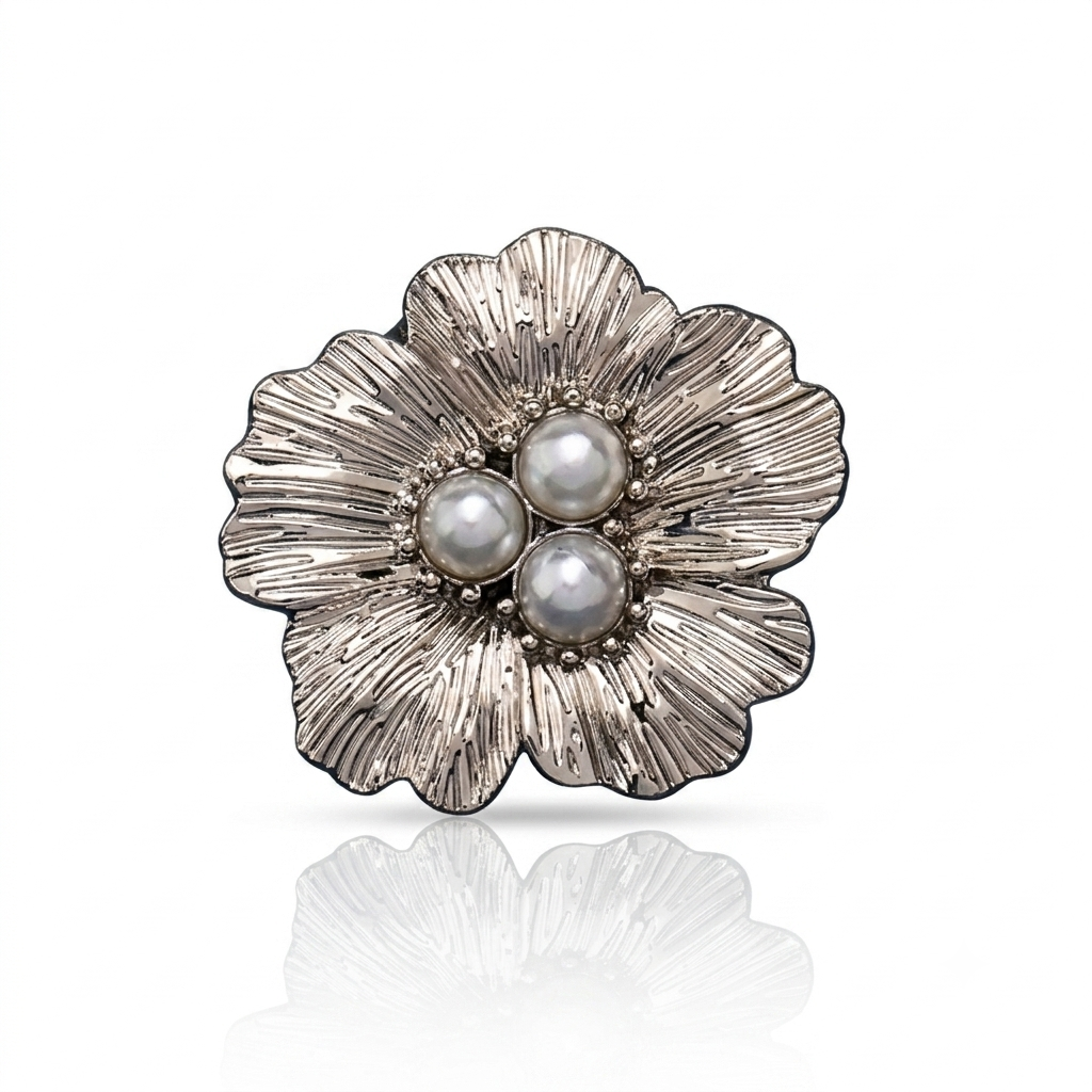 A silver-tone flower-shaped brooch with three white pearls at the center, displayed on a clean white background with a soft reflection below.