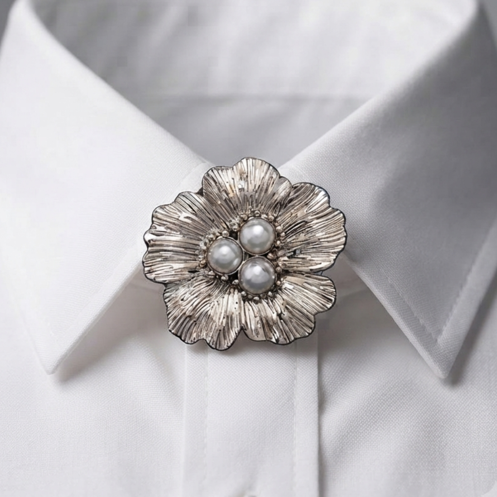 A silver-toned flower-shaped brooch with three white faux pearls in the center, pinned to the collar of a white dress shirt.