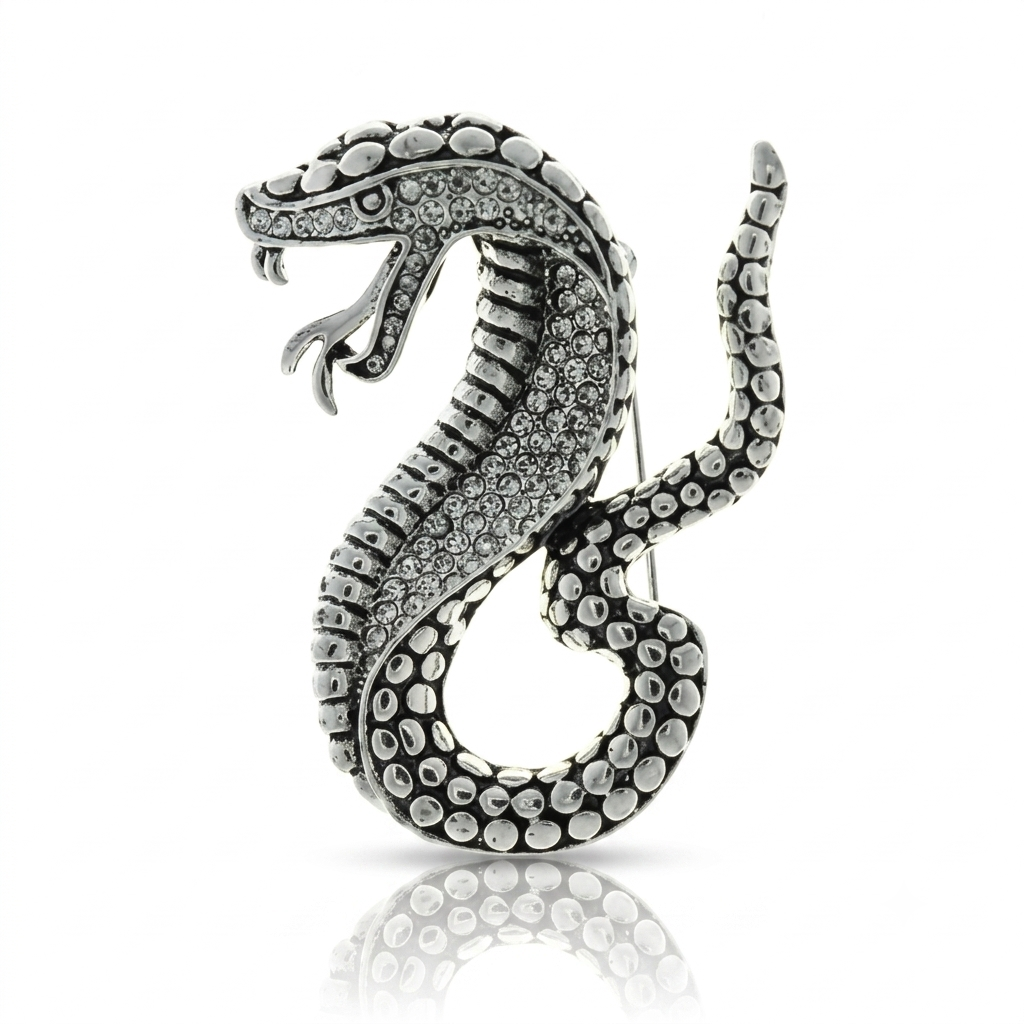 A silver snake-shaped brooch or pin, detailed with small clear rhinestones and textured raised sections, shown on a white background with a soft reflection below.