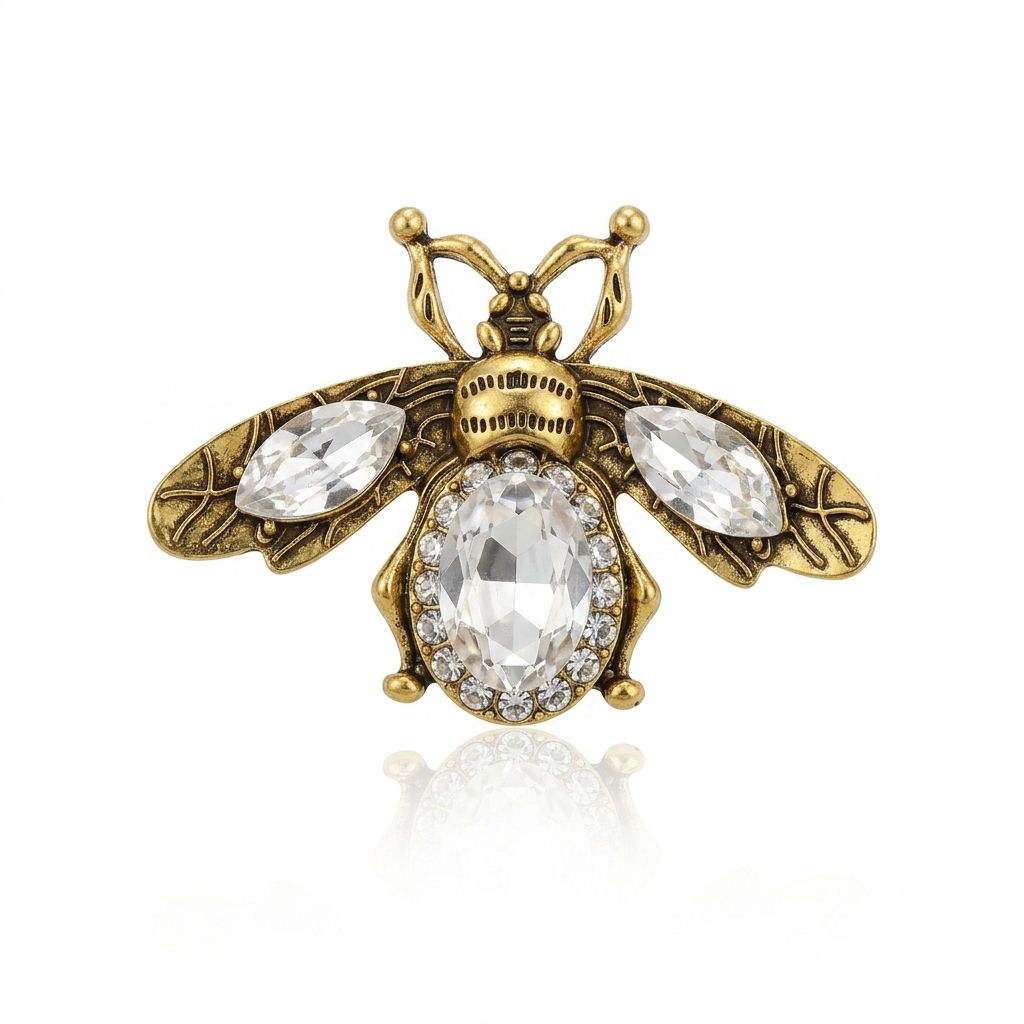 An antique gold bee brooch featuring a large oval clear crystal in the center, surrounded by a halo of small clear crystals, with two marquise-shaped clear crystals on the wings. The wings and body are detailed with engraved leaf patterns.