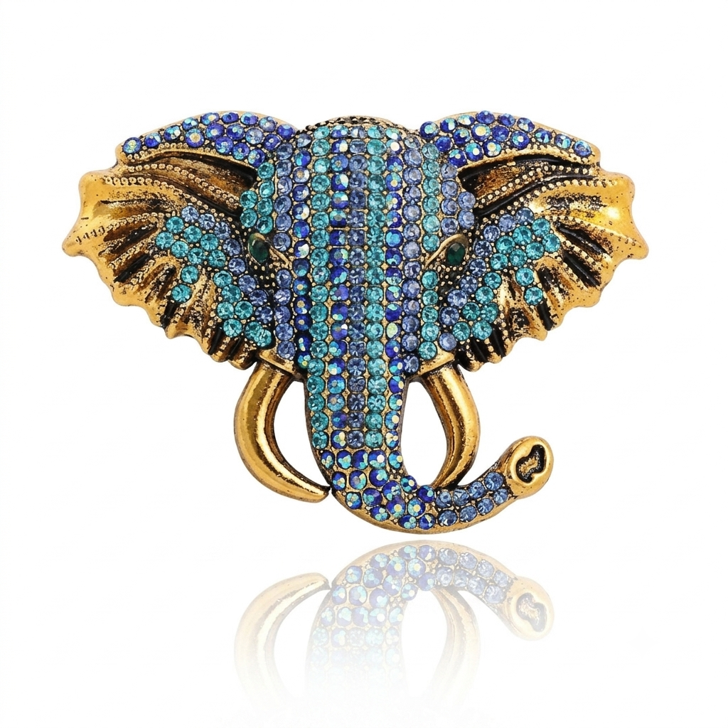 An elephant-shaped brooch or pin with gold-tone metal and rows of blue, teal, and iridescent rhinestones, shown on a white background with a soft reflection below.