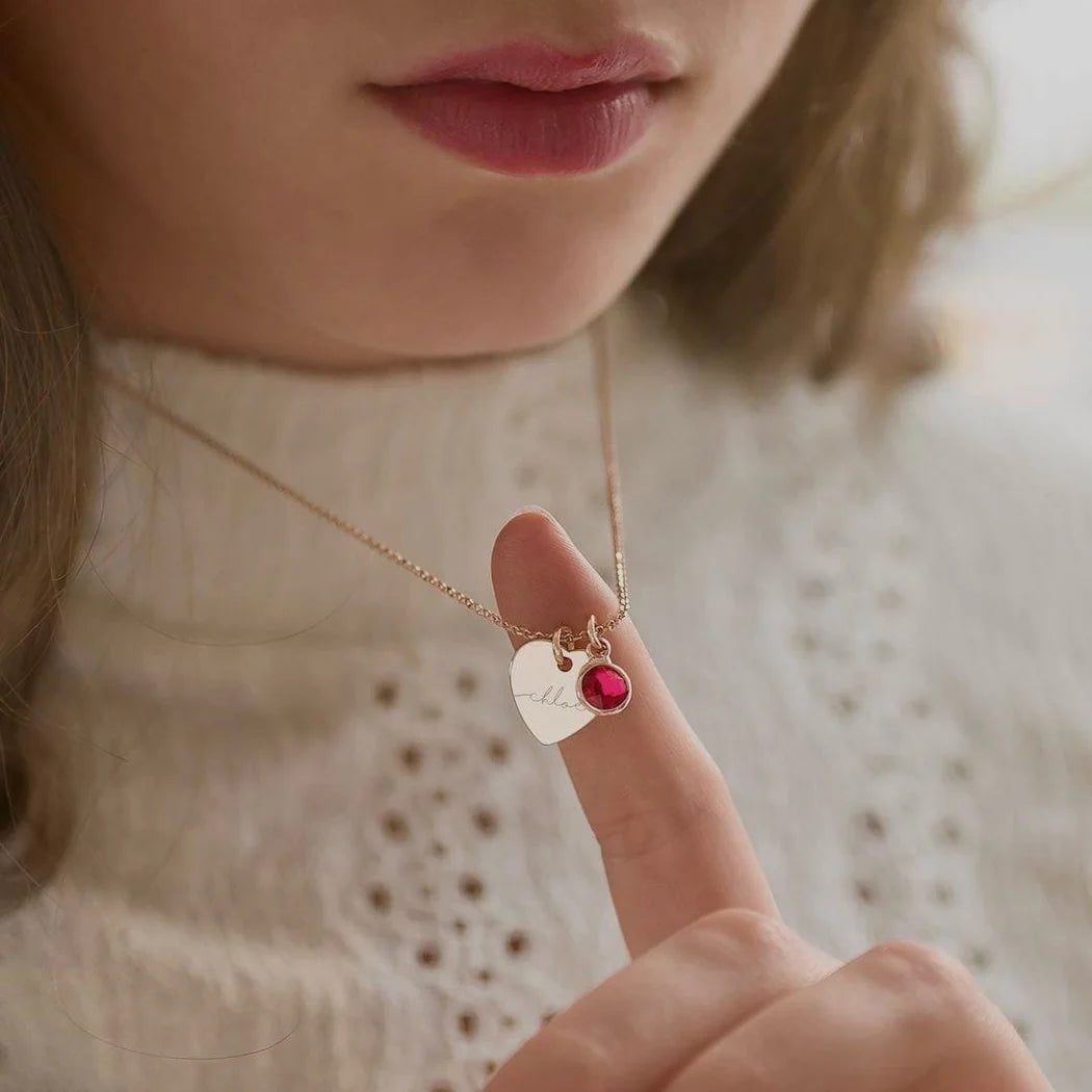 Close-up of a person wearing a delicate necklace with a heart-shaped pendant and red gemstone.