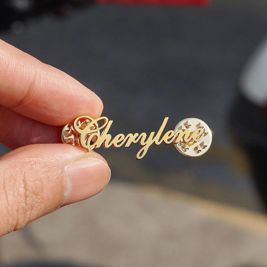 Gold earrings with 'Cherylee' inscription held by a hand against a blurred background