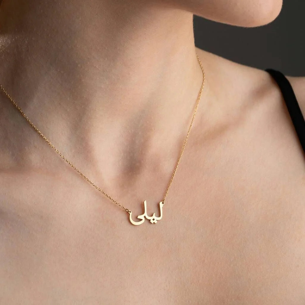 Gold necklace with Arabic script on a person's neck against a neutral background