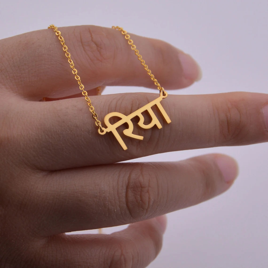 Gold necklace with a name pendant on a hand against a plain background