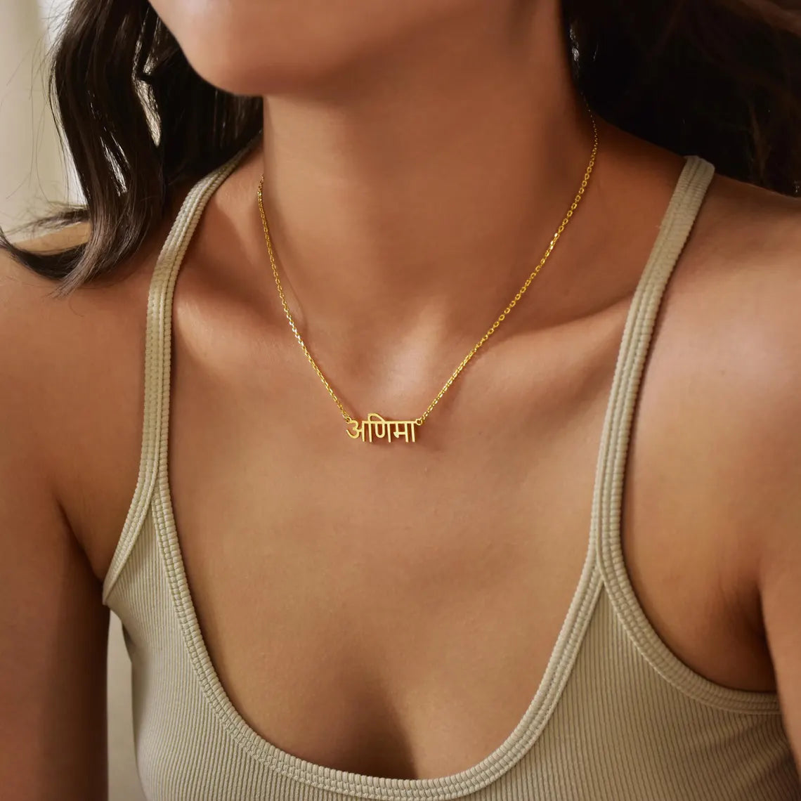 Gold necklace with a nameplate worn by a person in a beige tank top.