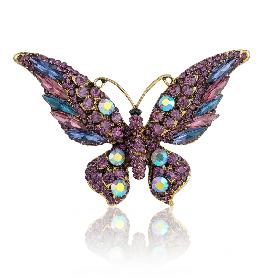 A butterfly-shaped brooch with gold-tone metal outlines and pavé-set purple crystals, accented with iridescent blue, pink, and yellow rhinestones, shown on a white background with a soft reflection below.