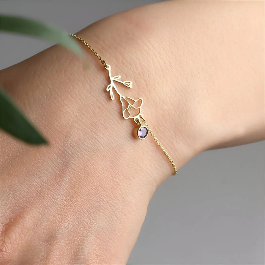 Gold bracelet with a purple gemstone on a wrist against a gray background