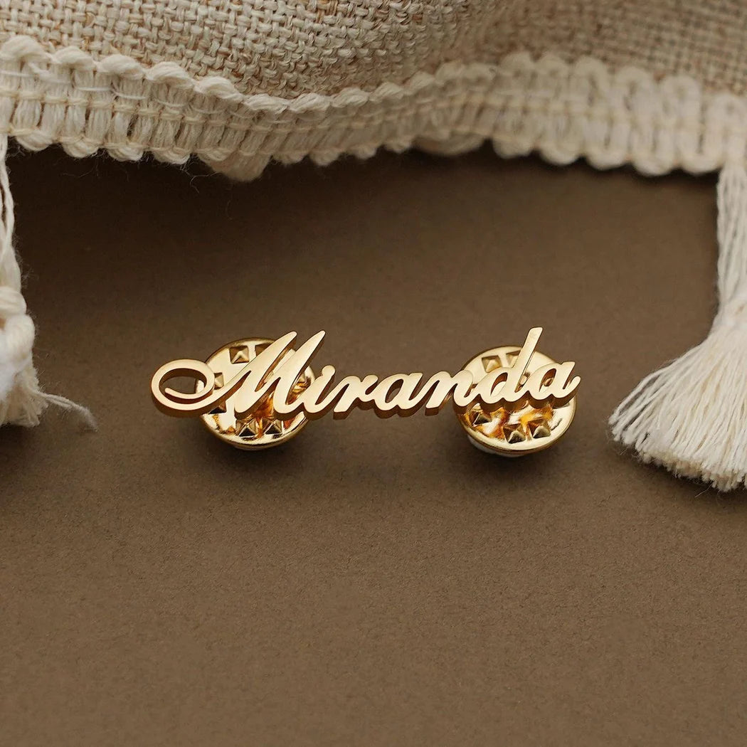 Gold earrings with 'Miranda' on a textured surface