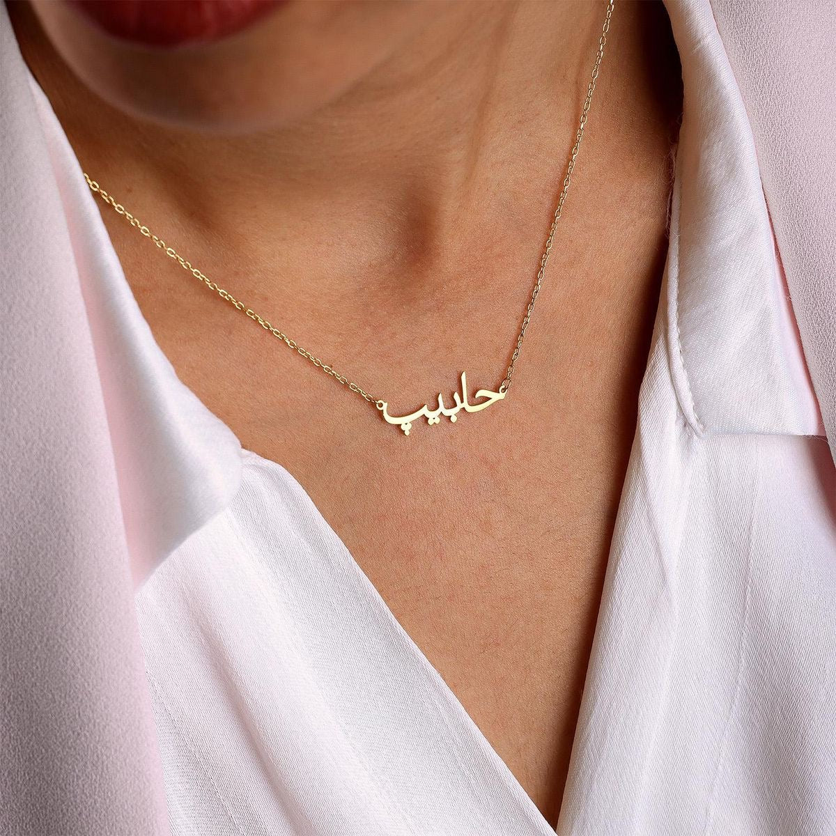 Gold necklace with Arabic script worn by a person in a white shirt