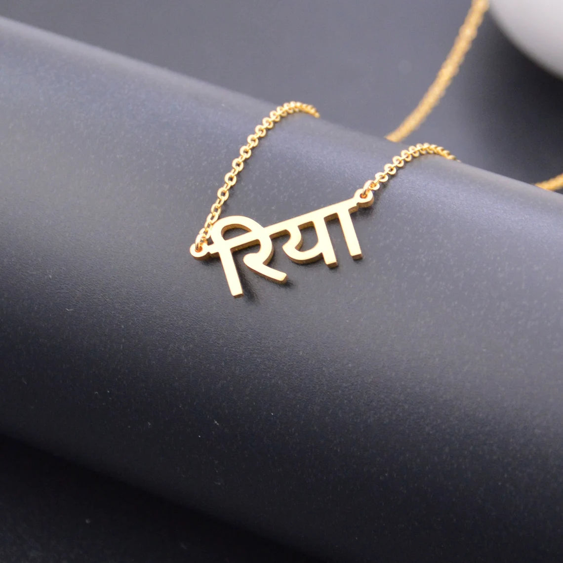 Gold necklace with a name pendant on a dark surface