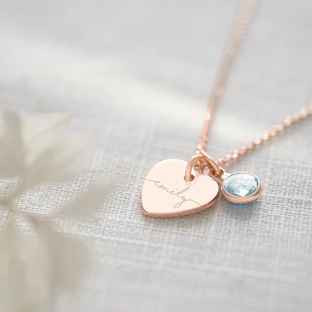 Rose gold necklace with heart-shaped pendant and blue gemstone on a textured fabric background