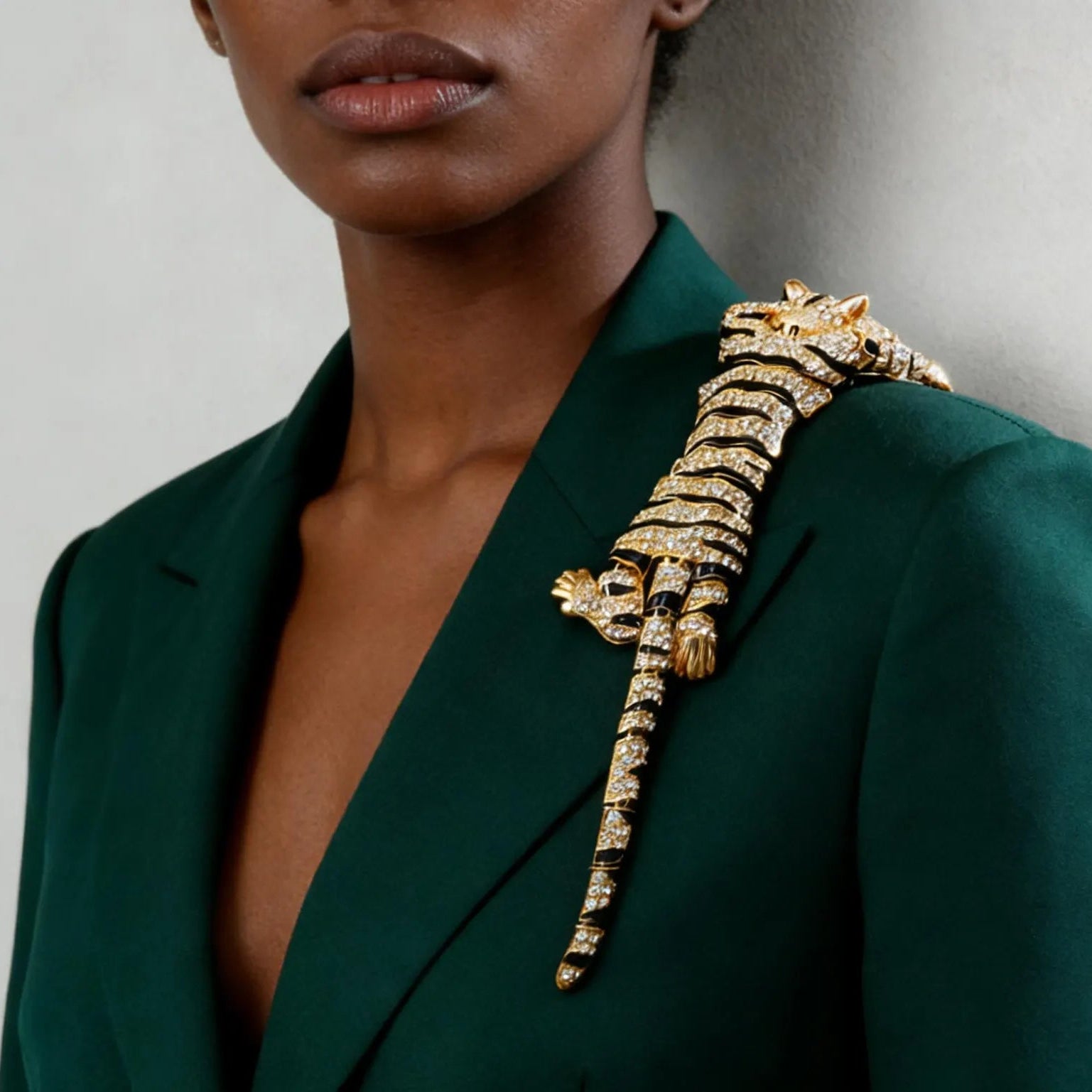 A close-up of a model wearing a large, gold tiger-shaped brooch embellished with clear crystals on the lapel of a dark green blazer.